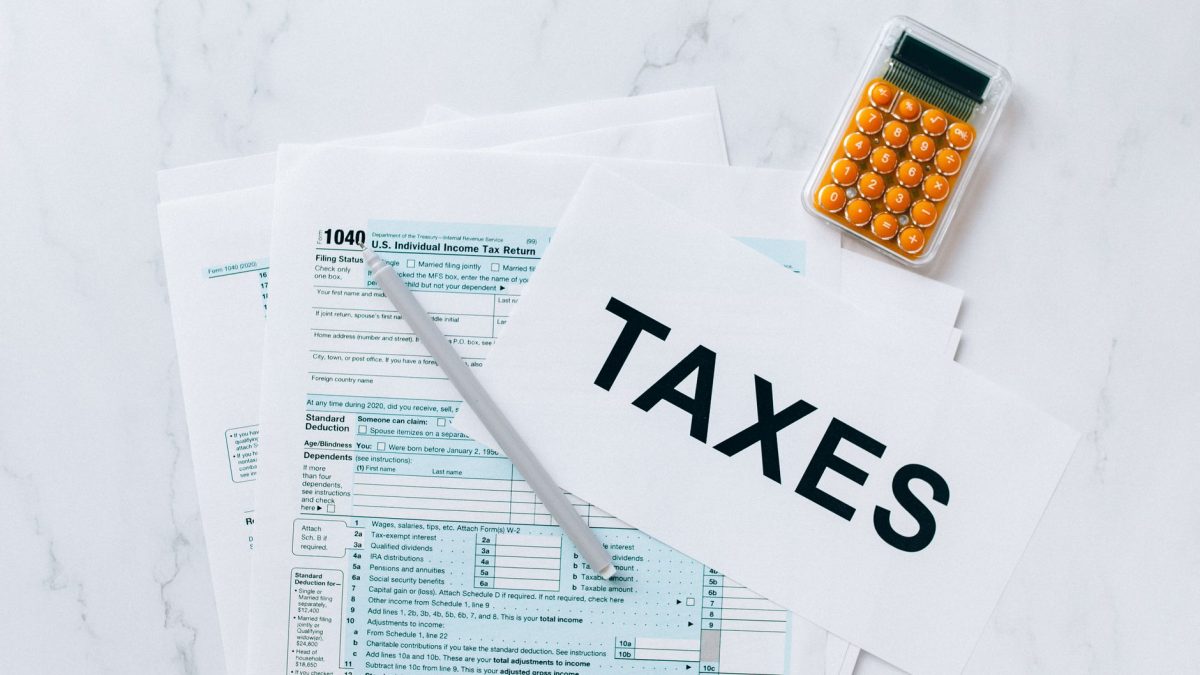 Formulários tributários, calculadora e caneta sobre uma mesa, representando a preparação de documentos para questões fiscais.