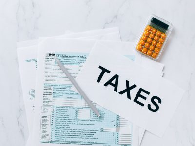 Formulários tributários, calculadora e caneta sobre uma mesa, representando a preparação de documentos para questões fiscais.
