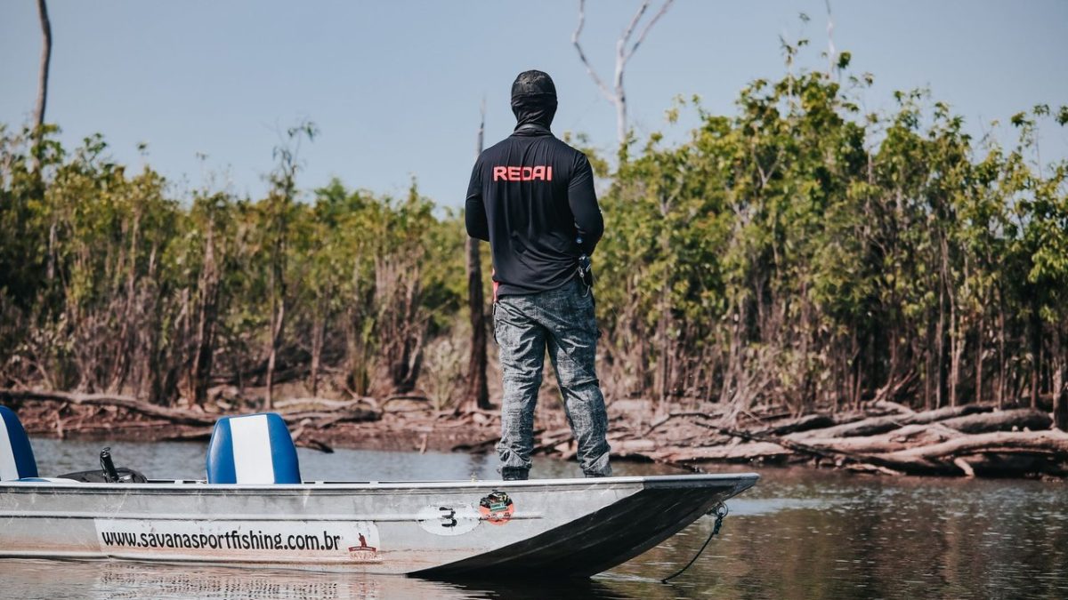 Pescador em um barco no Rio Negro, cercado pela vegetação da floresta amazônica.