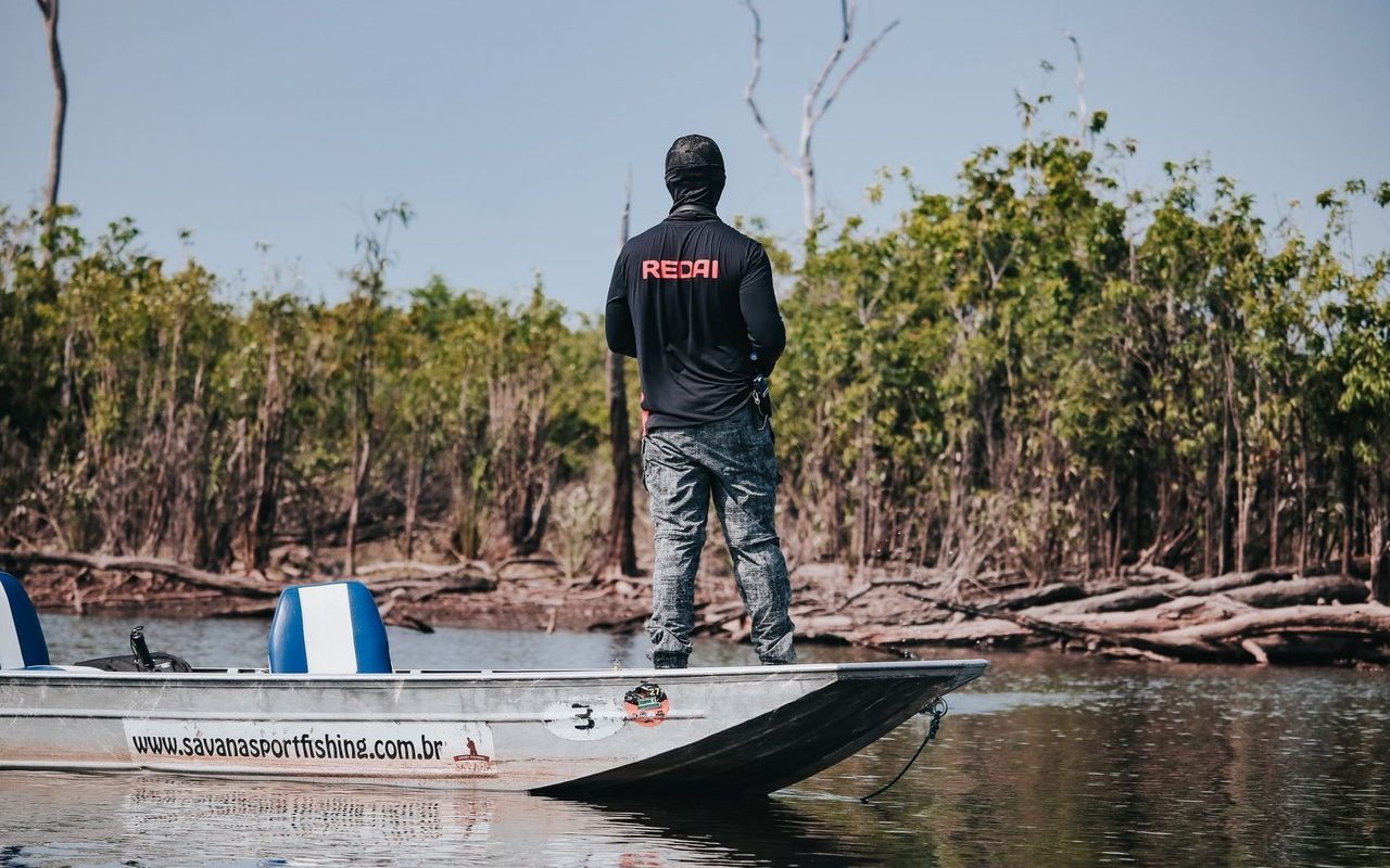 Pescador em um barco no Rio Negro, cercado pela vegetação da floresta amazônica.