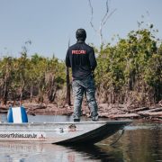 Pescador em um barco no Rio Negro, cercado pela vegetação da floresta amazônica.