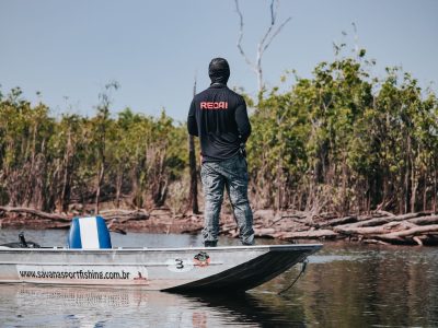 Pescador em um barco no Rio Negro, cercado pela vegetação da floresta amazônica.