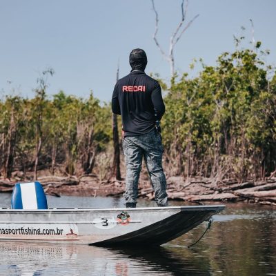 Pescador em um barco no Rio Negro, cercado pela vegetação da floresta amazônica.