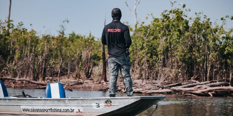 Pescador em um barco no Rio Negro, cercado pela vegetação da floresta amazônica.