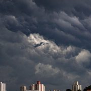Nuvens escuras se acumulam sobre prédios de uma área urbana, indicando a aproximação de uma tempestade.