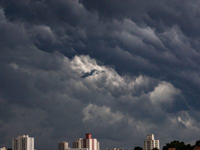Nuvens escuras se acumulam sobre prédios de uma área urbana, indicando a aproximação de uma tempestade.