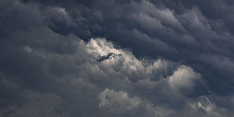 Nuvens escuras se acumulam sobre prédios de uma área urbana, indicando a aproximação de uma tempestade.