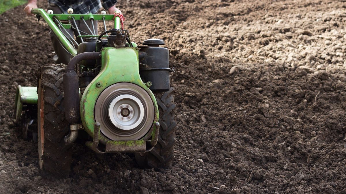 Agricultor opera um trator compacto em um campo recém-arado durante o preparo do solo para o plantio.