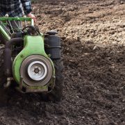 Agricultor opera um trator compacto em um campo recém-arado durante o preparo do solo para o plantio.