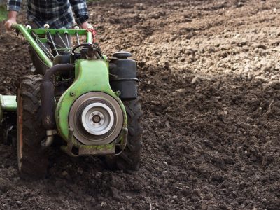 Agricultor opera um trator compacto em um campo recém-arado durante o preparo do solo para o plantio.